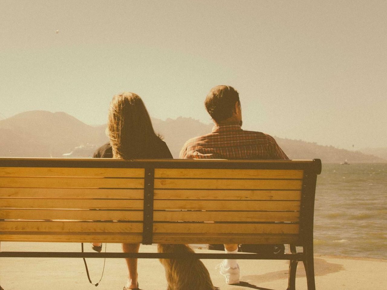 Two people sitting close together on a bench by the water