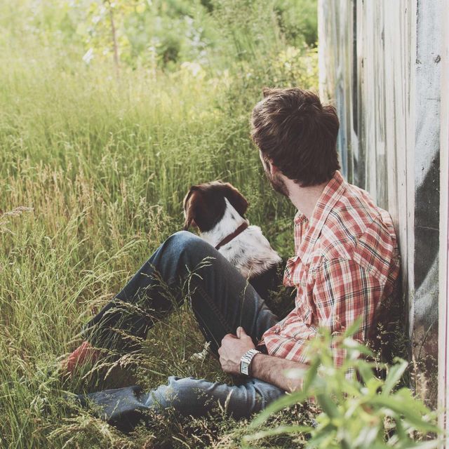 A man resting in long grass next to his dog